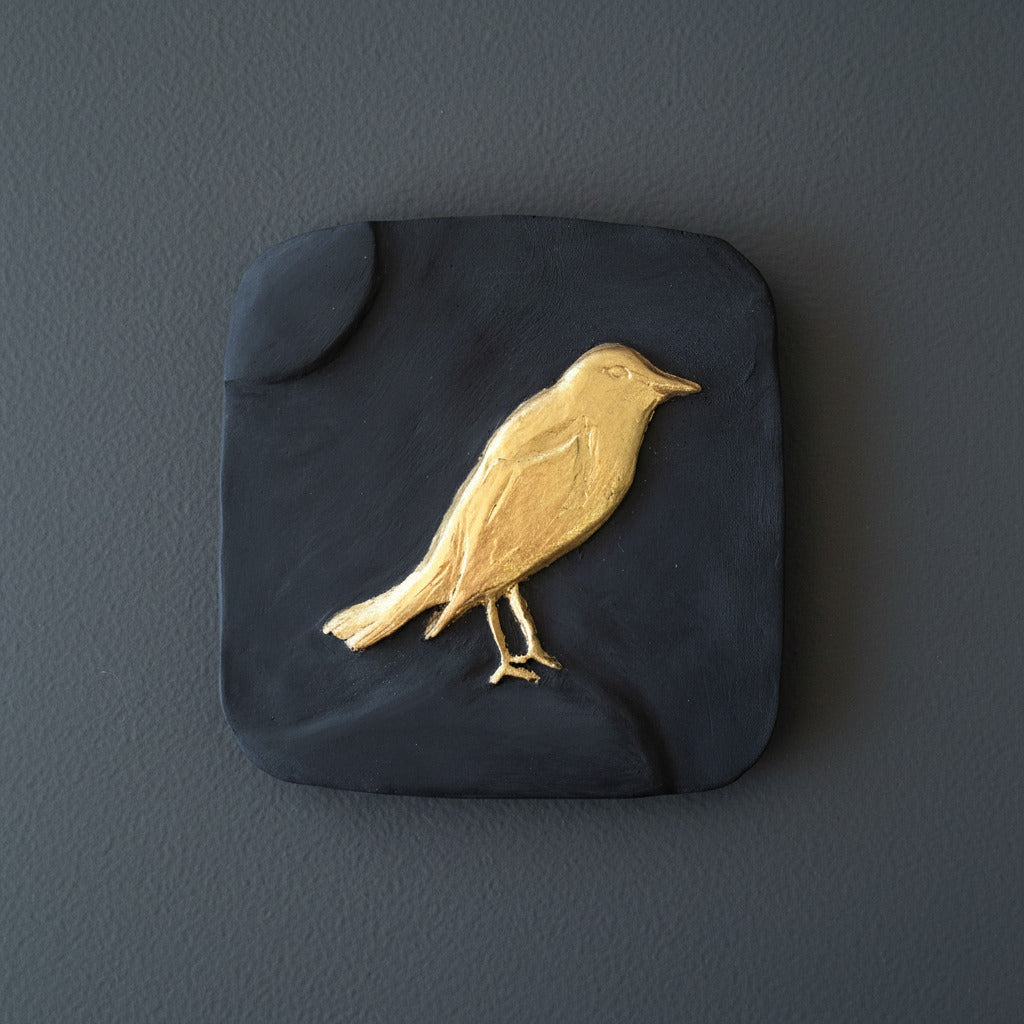 Gold bird design on a dark blue square stone coaster on a wooden surface